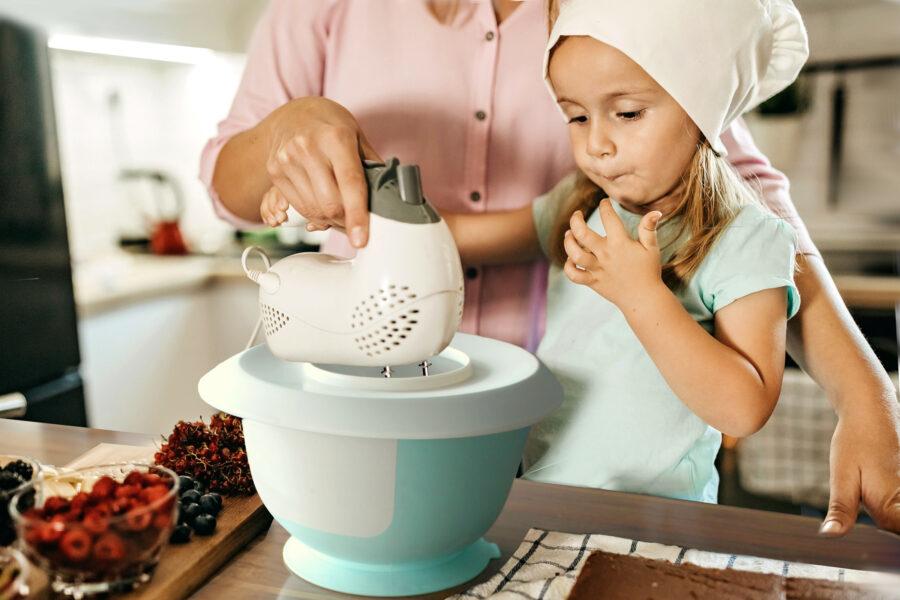 A child stirs cake batter in a mixing bowl using a hand mixer.