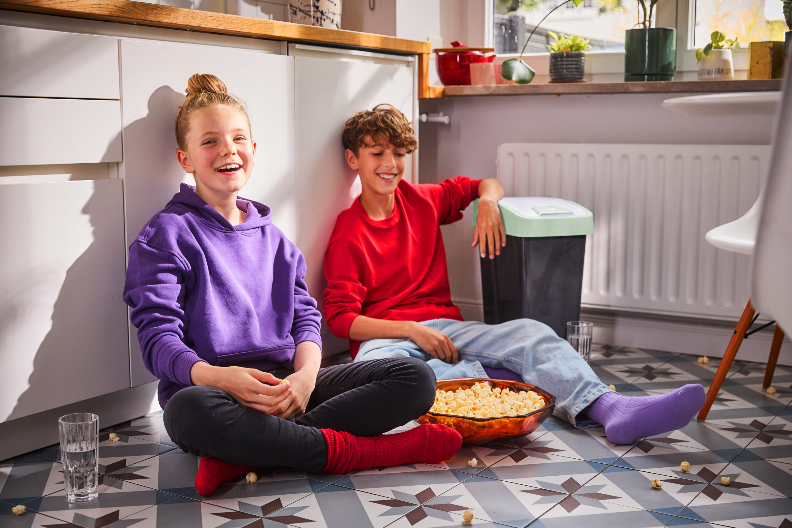 Zwei Kinder sitzen lachend in der Küche neben dem modernen keeeper Abfalleimer magne – praktische Lösung für hygienische Mülltrennung, komfortable Handhabung und mehr Ordnung im familienfreundlichen Zuhause.
