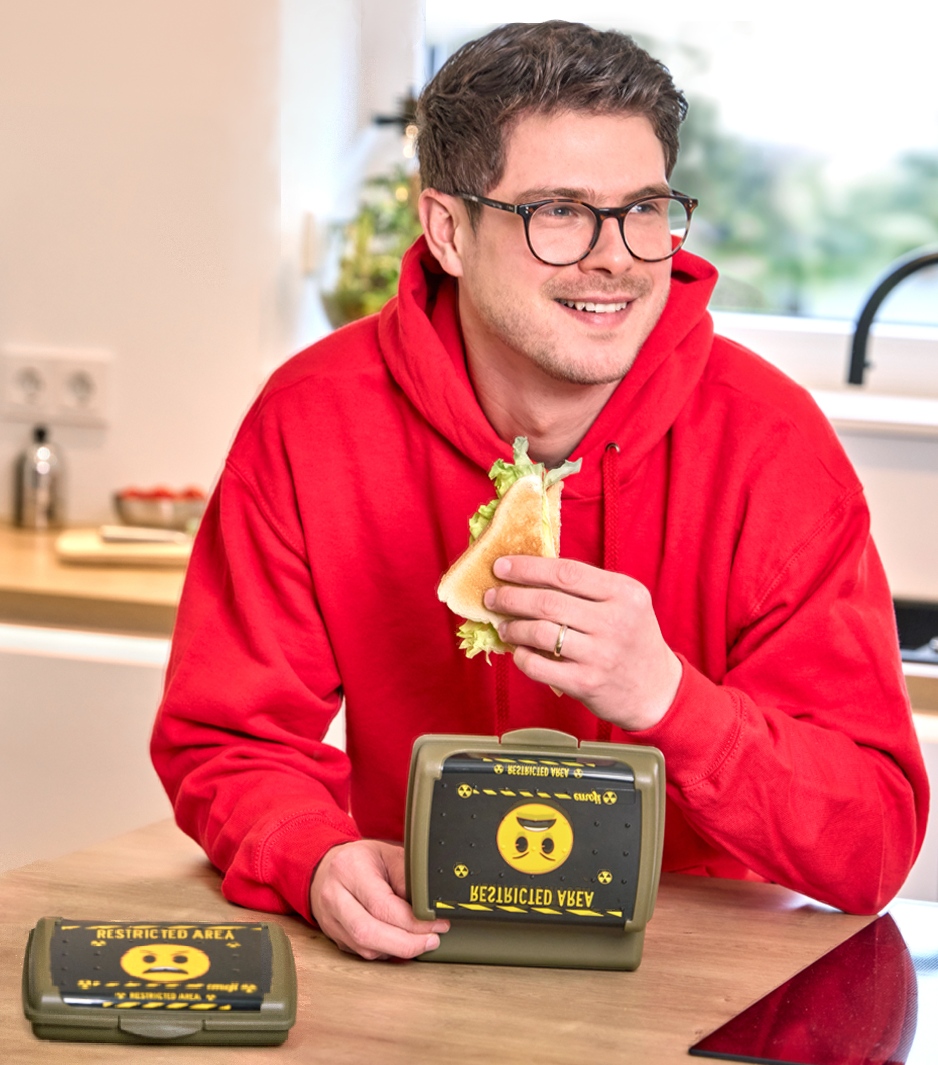 keeeper carla lunch box with emoji danger design, held by a man eating a sandwich.