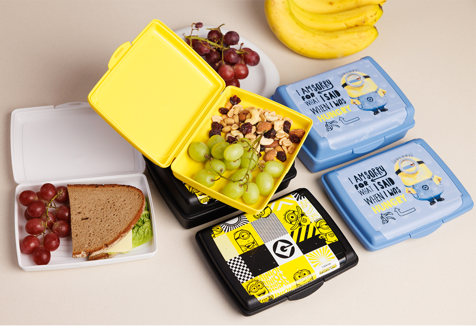 Open lunchboxes with snacks like grapes, nuts, and a sandwich, alongside closed Minions-themed boxes.