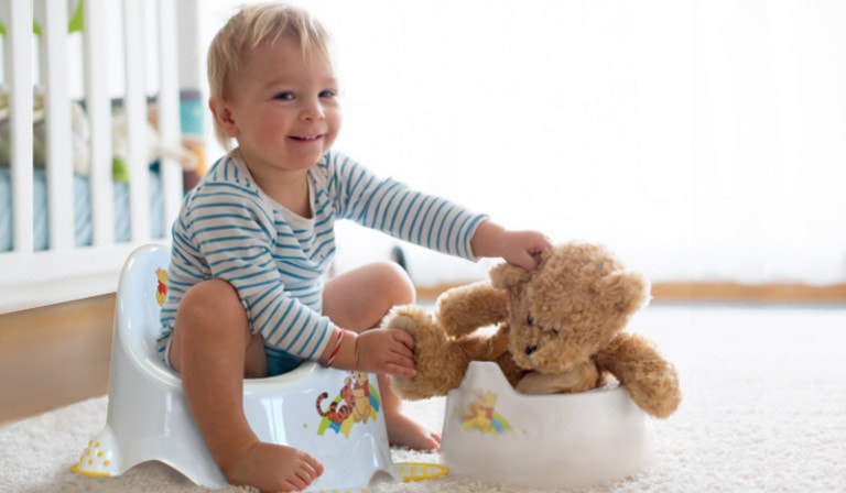 Ein Baby sitzt auf dem Töpfchen, spielt mit dem Teddy.
